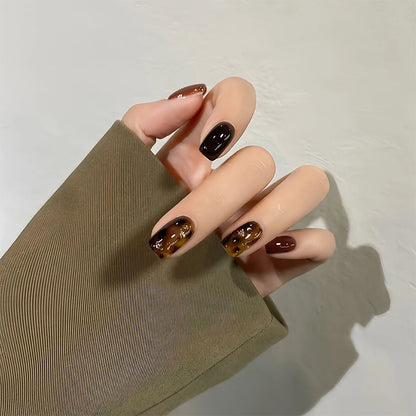 Hand with tortoiseshell nail design on a plain background