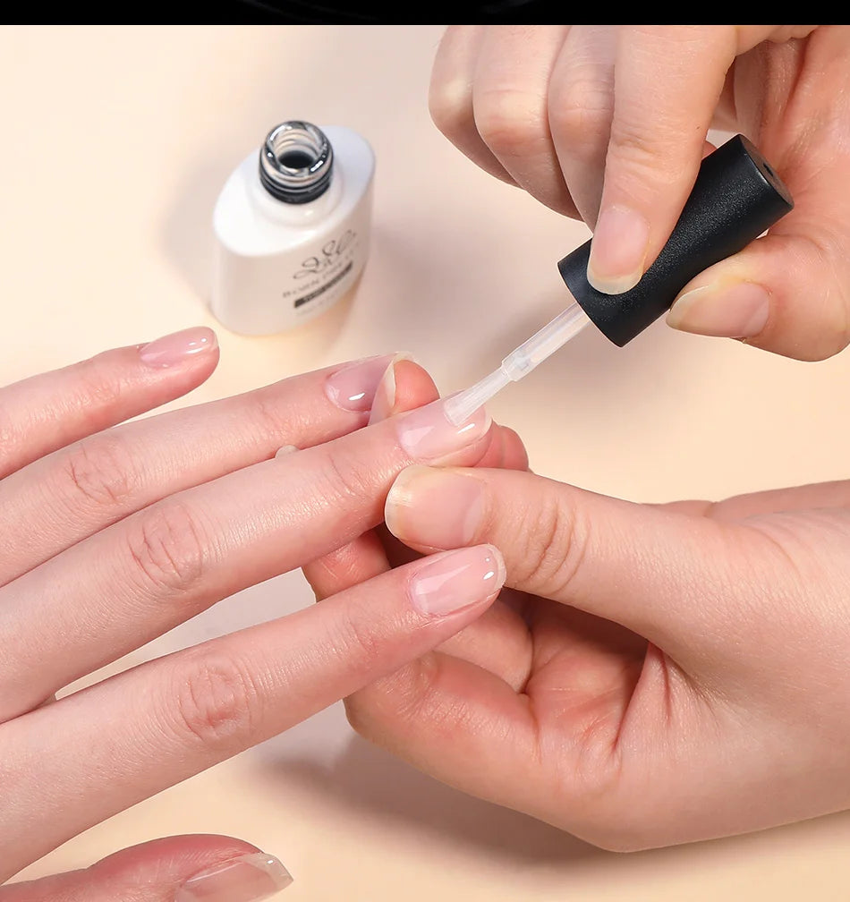 Person applying nail polish to another person's fingernail with a bottle of nail polish in the background.